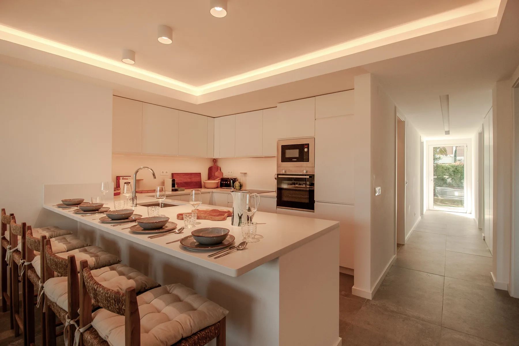 A bright kitchen and dining area features a long island with seating and a hallway beyond.