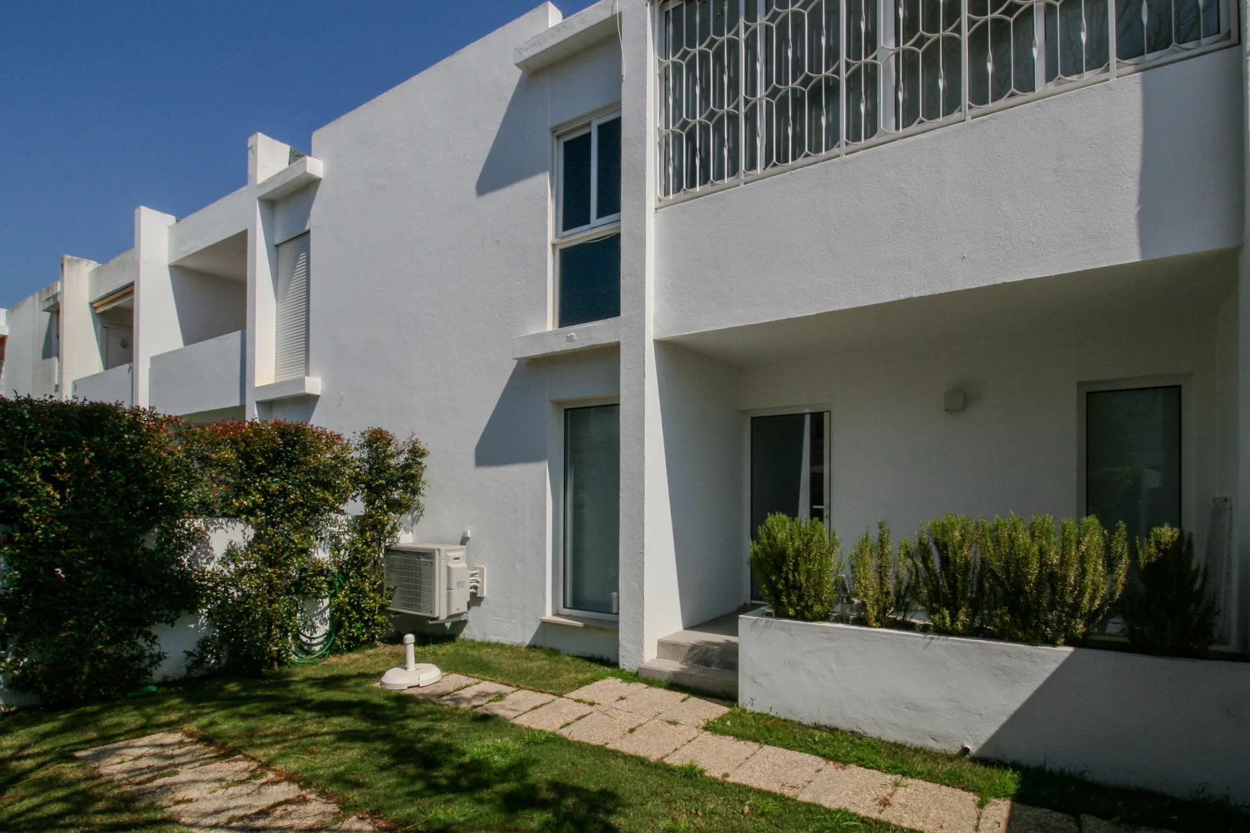 White apartment building with a small garden and paved walkway in front.