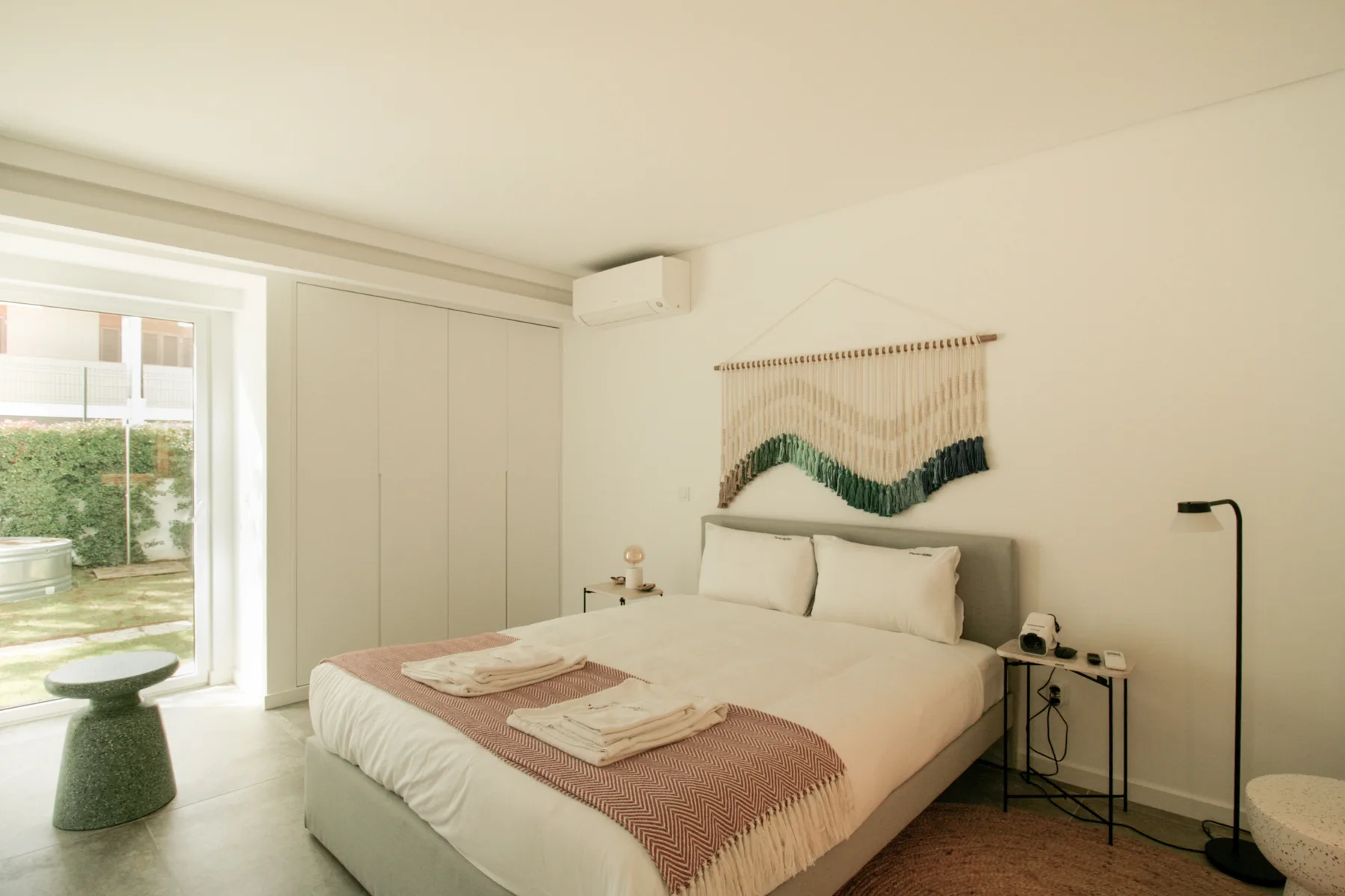 A bedroom with a neatly made bed and woven wall hanging.