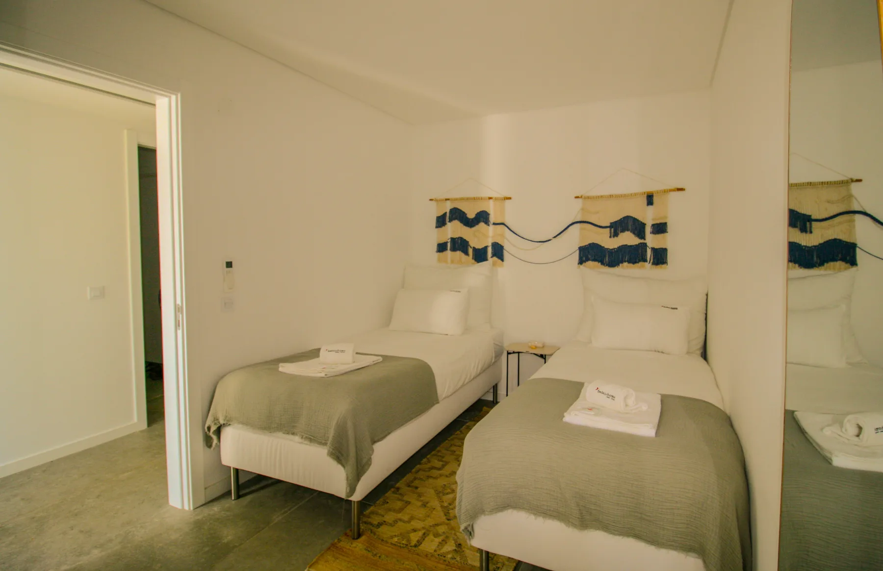A bedroom with two beds, gray bedding, and blue-and-white wall hangings.