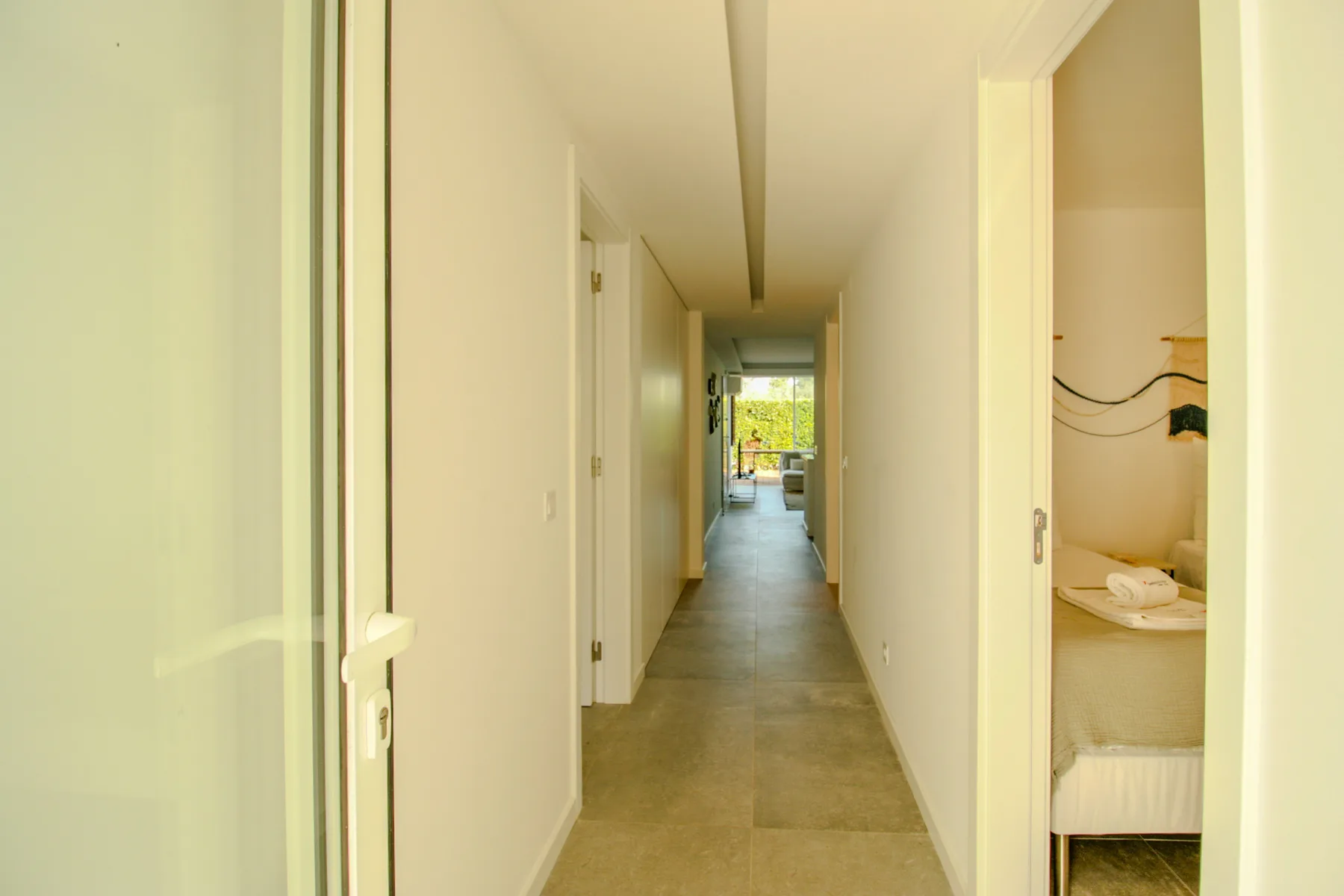 A bright hallway leads toward a room with a bed and a window.