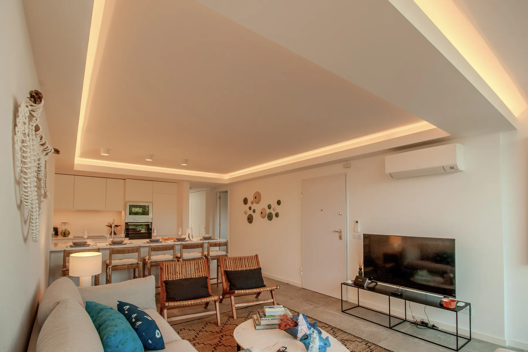 A bright living room with seating, a television, and an open kitchen.