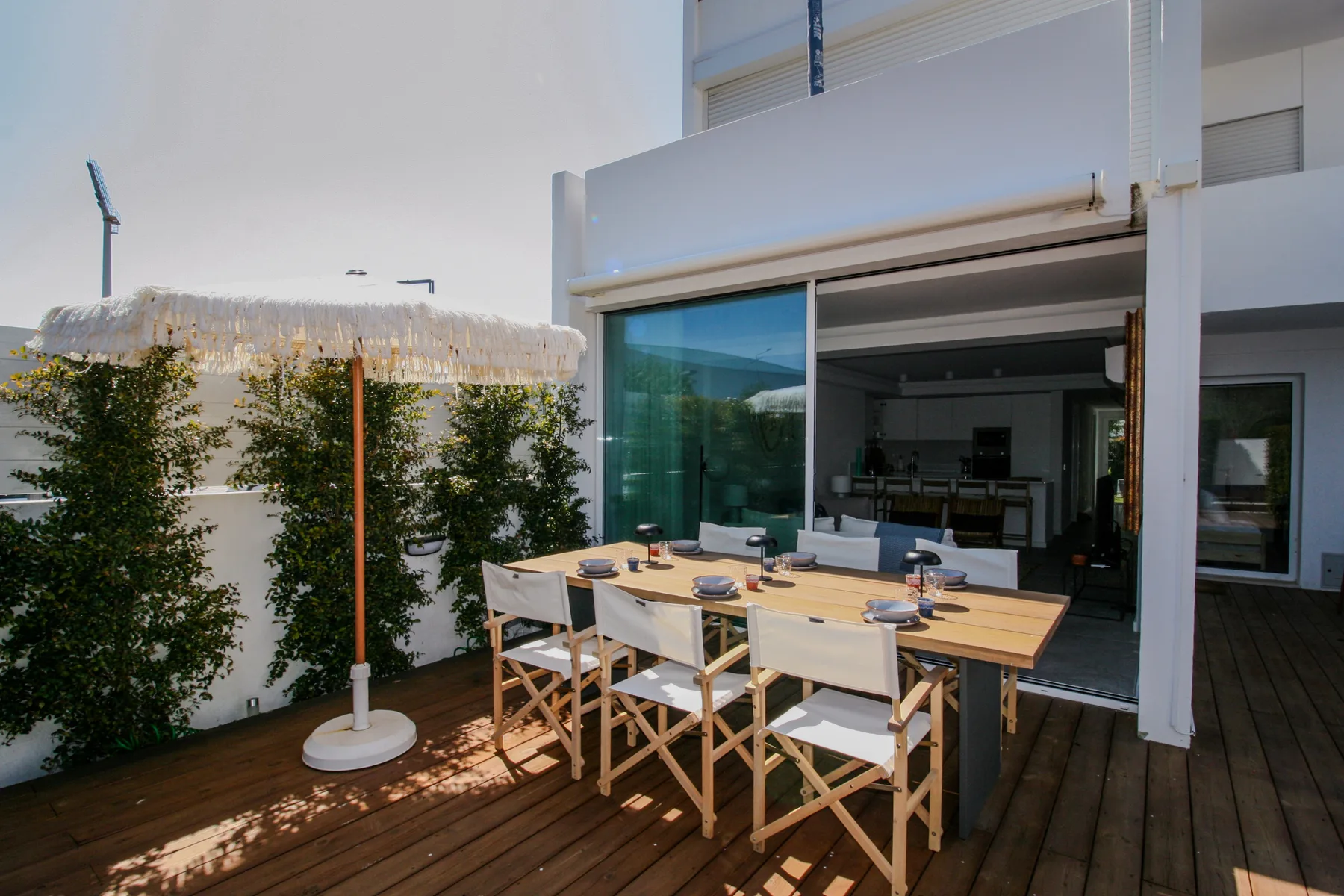 A wooden deck has an outdoor dining table beside a shaded seating area.