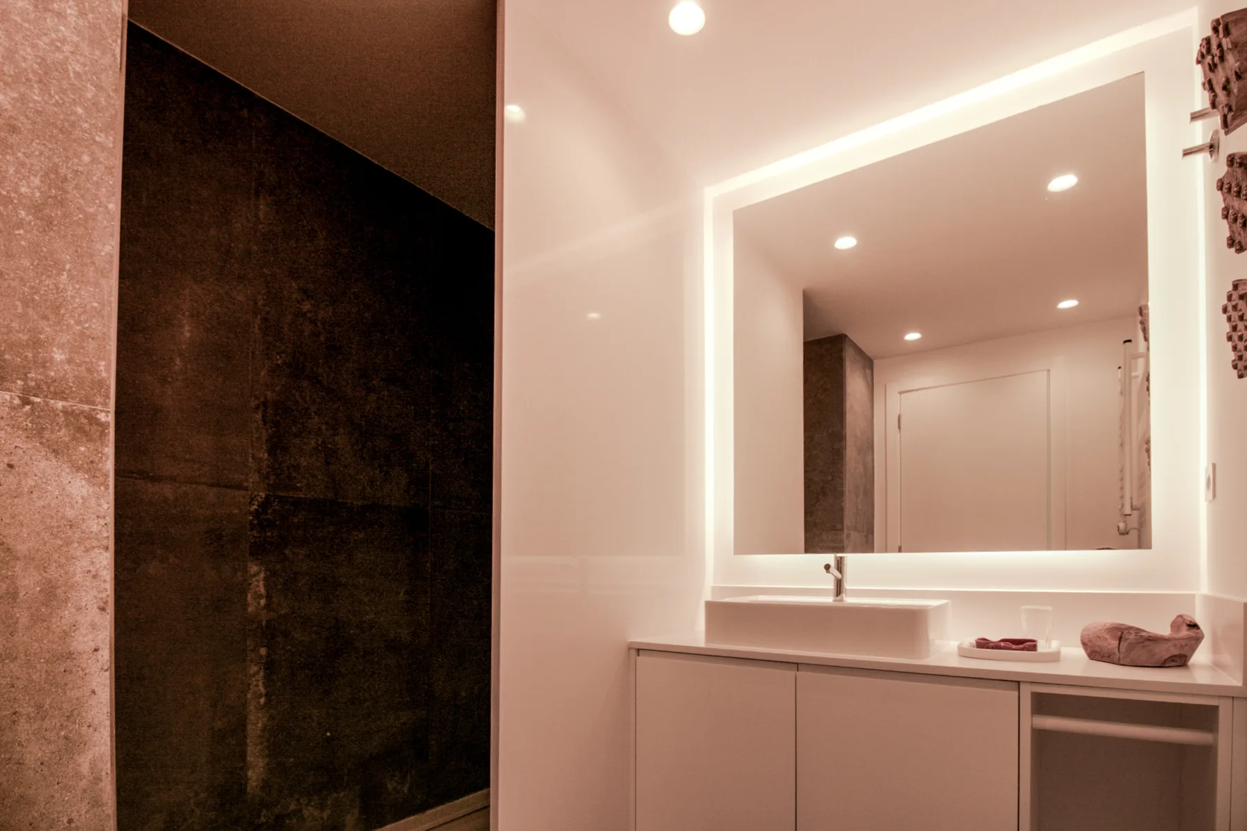 A bathroom vanity with a large mirror beside a dark shower.