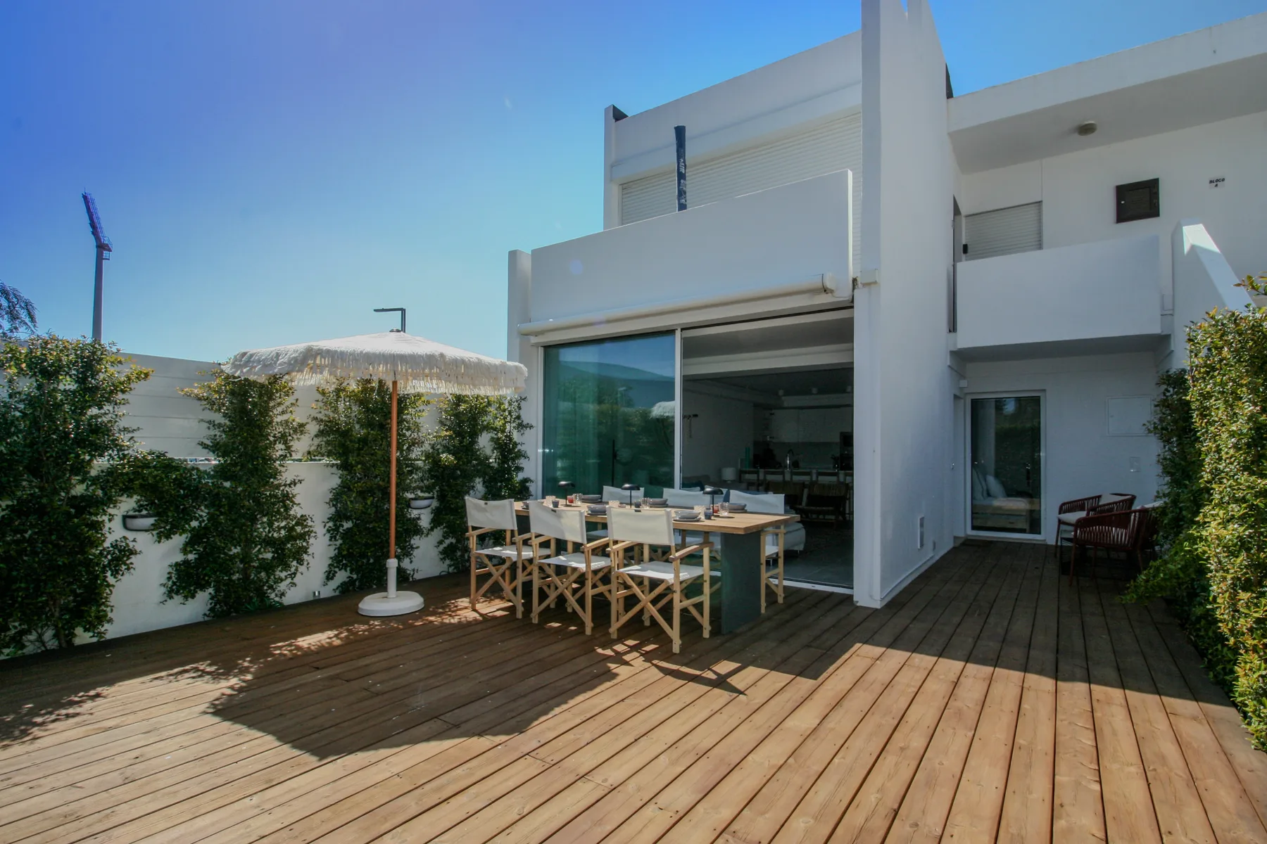 A wooden terrace with outdoor seating sits beside a modern white building.