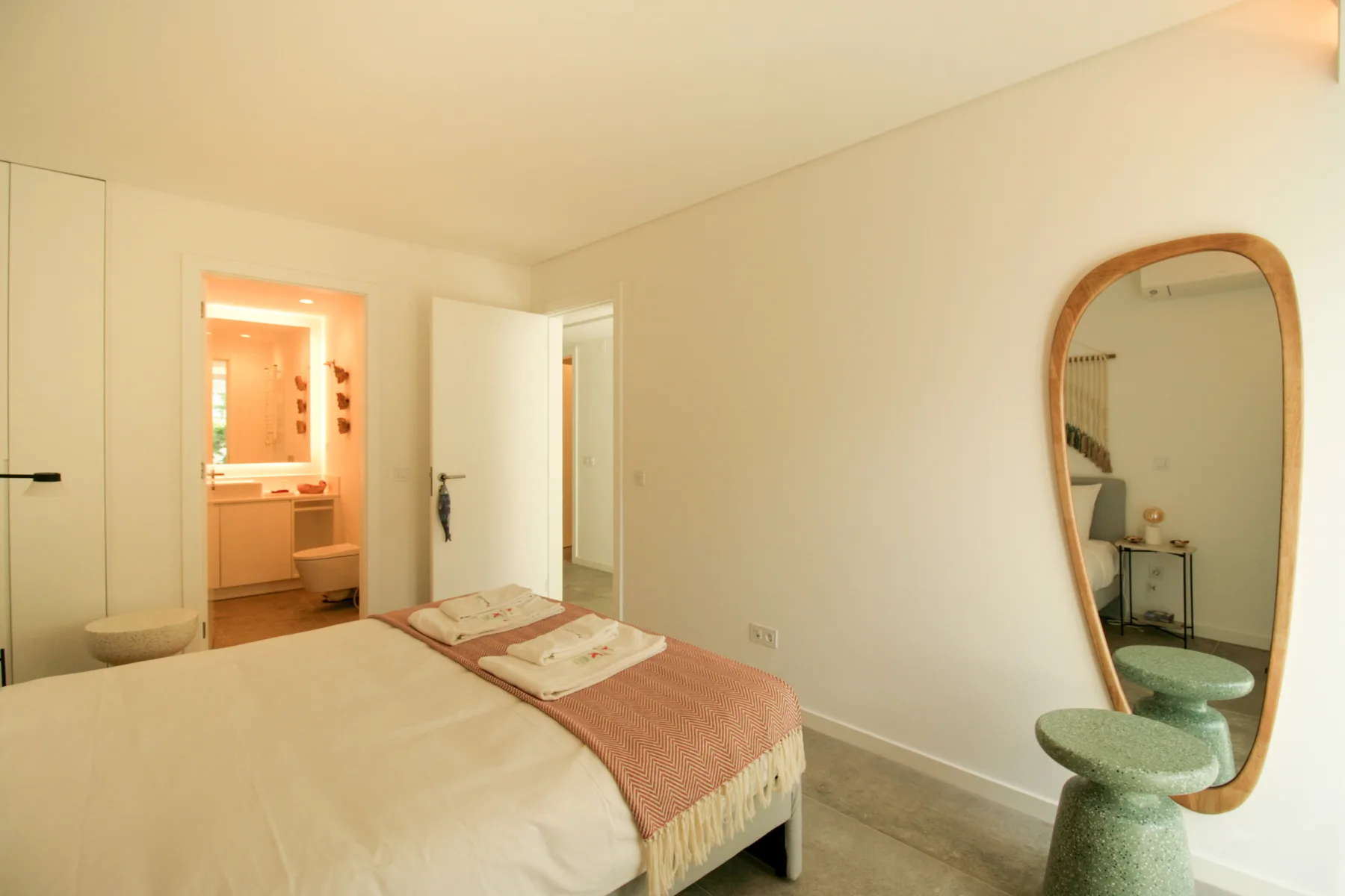 A bedroom with a bed, a mirror, and an open doorway to the bathroom.