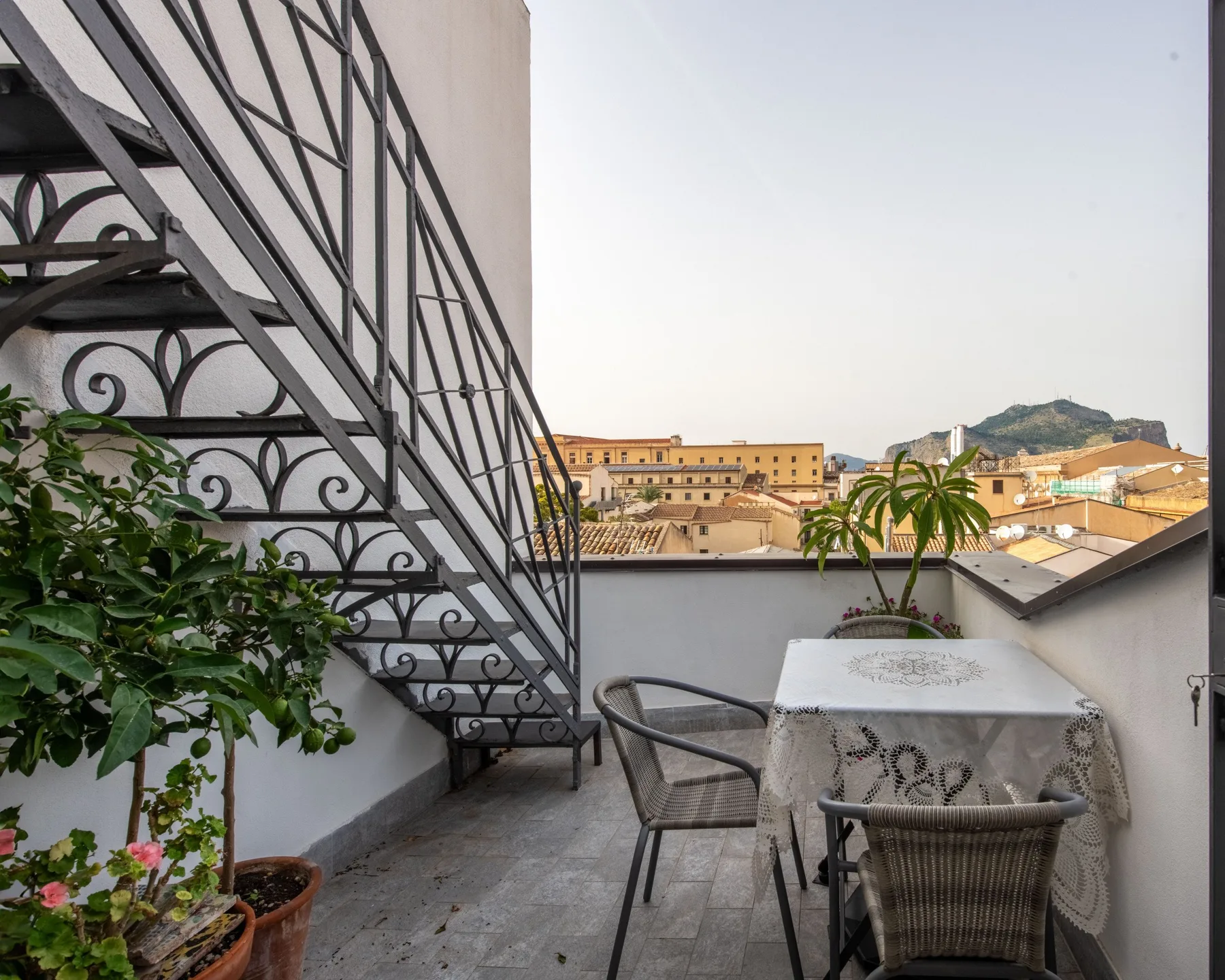 Una terraza en la azotea con una escalera metálica, una mesa y vistas de la ciudad.