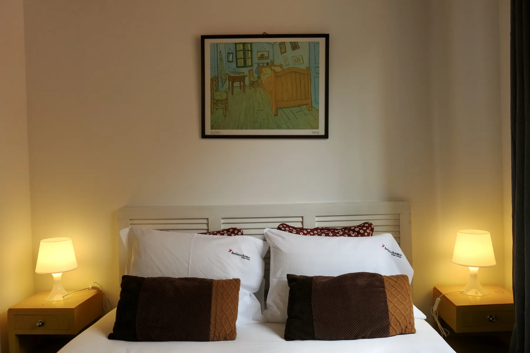 A bedroom with a white bed, brown cushions, bedside tables, and lamps.