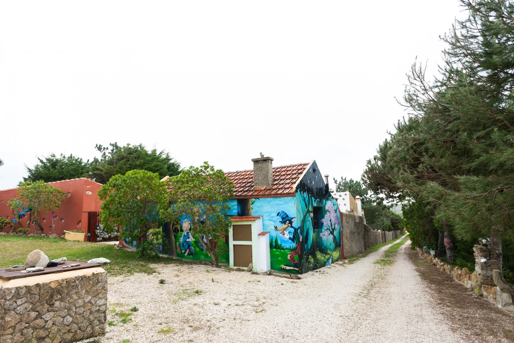 A gravel lane passes colorful buildings and trees.