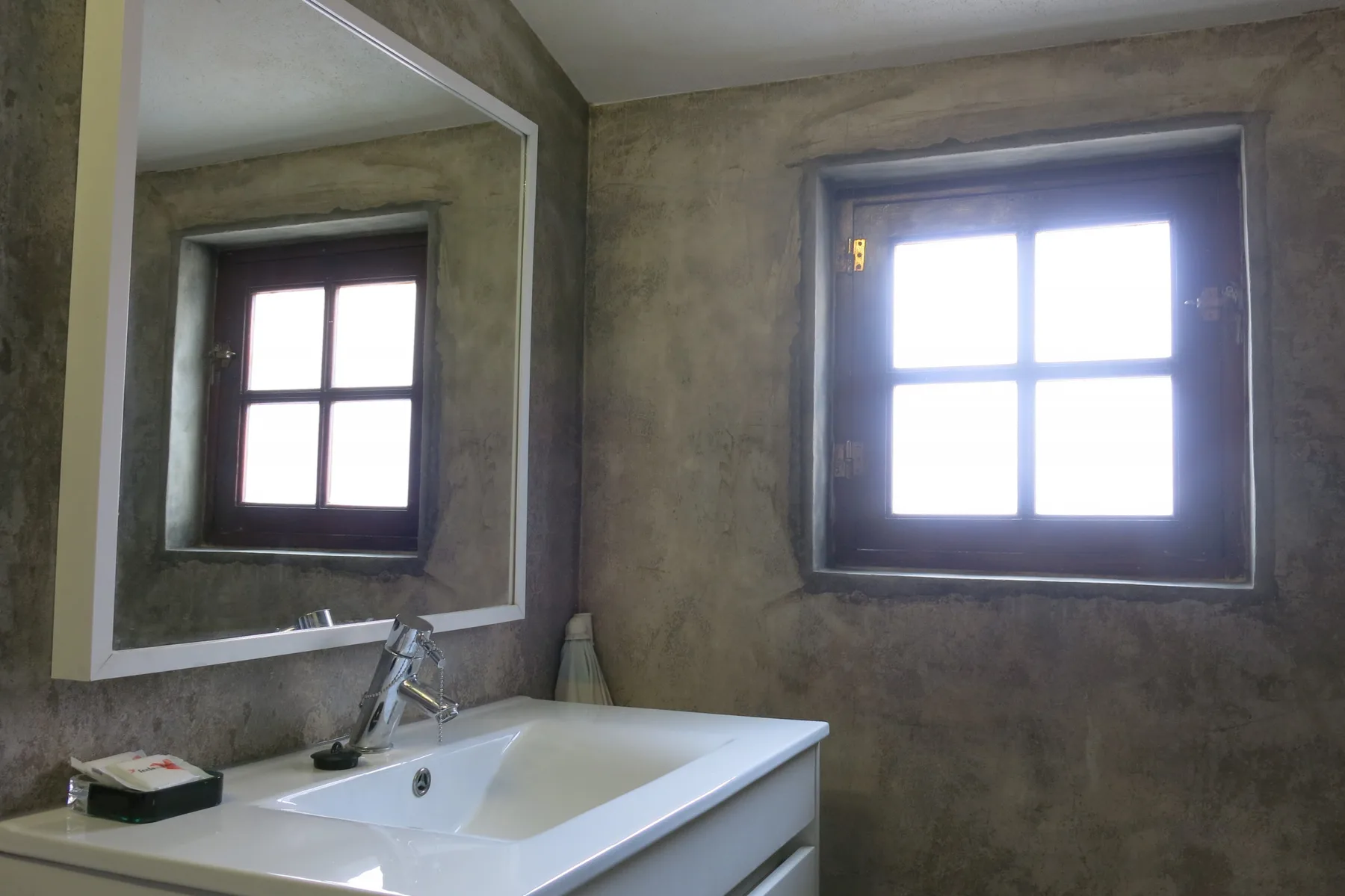 A bathroom vanity and mirror sit beneath a bright window.