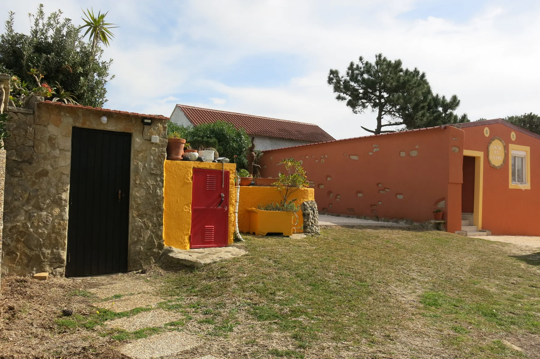 A courtyard with a red gate, stone walls, and a grassy yard.