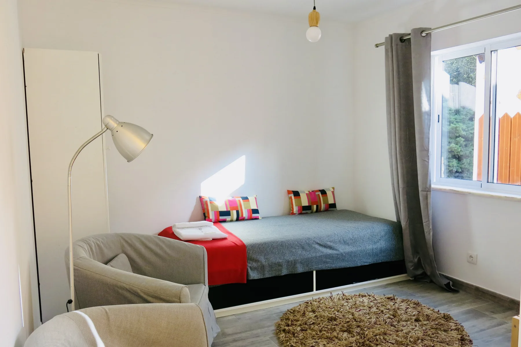 A bright bedroom with a bed, colorful pillows, and a window.