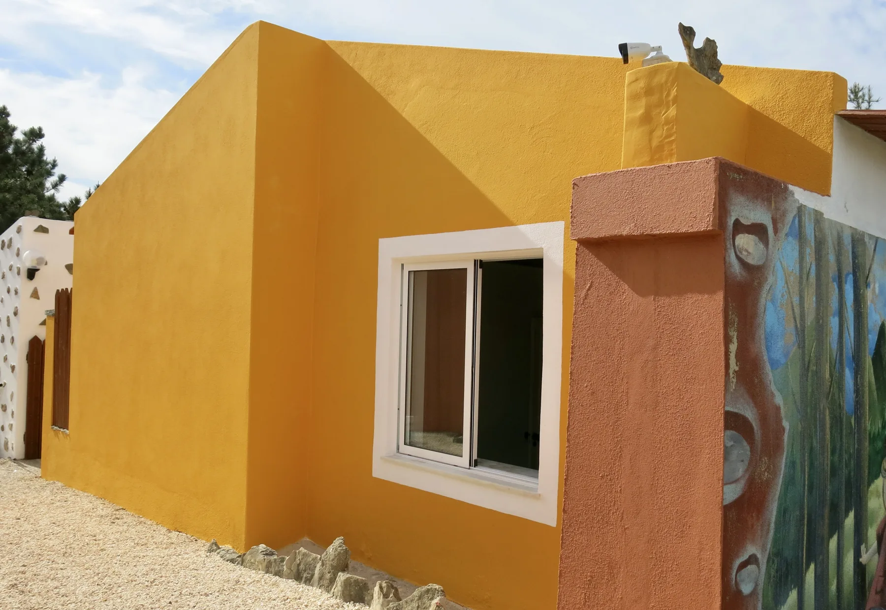 A bright yellow exterior wall has a white-framed window beside a painted gate.