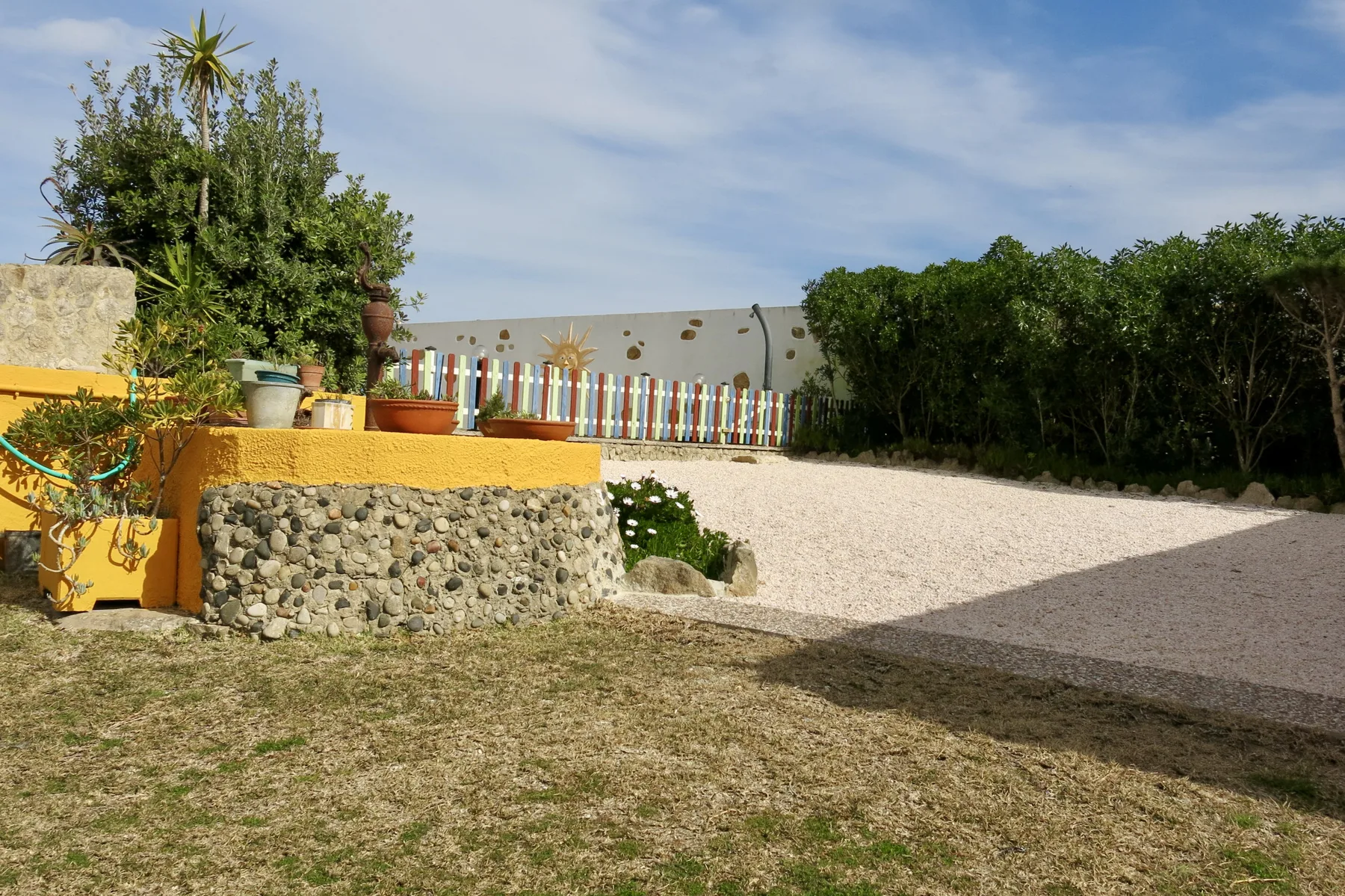 A gravel courtyard with a low stone planter and colorful fence.