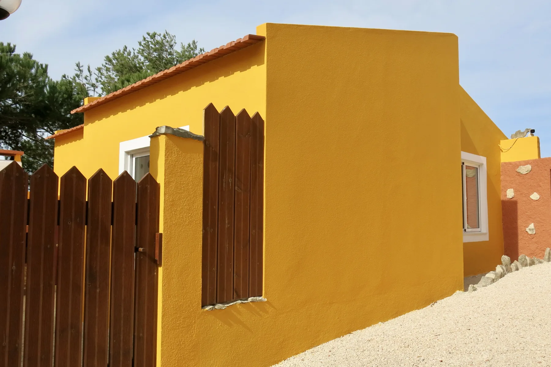 A mustard-yellow house with dark wooden fencing and a pale gravel path.
