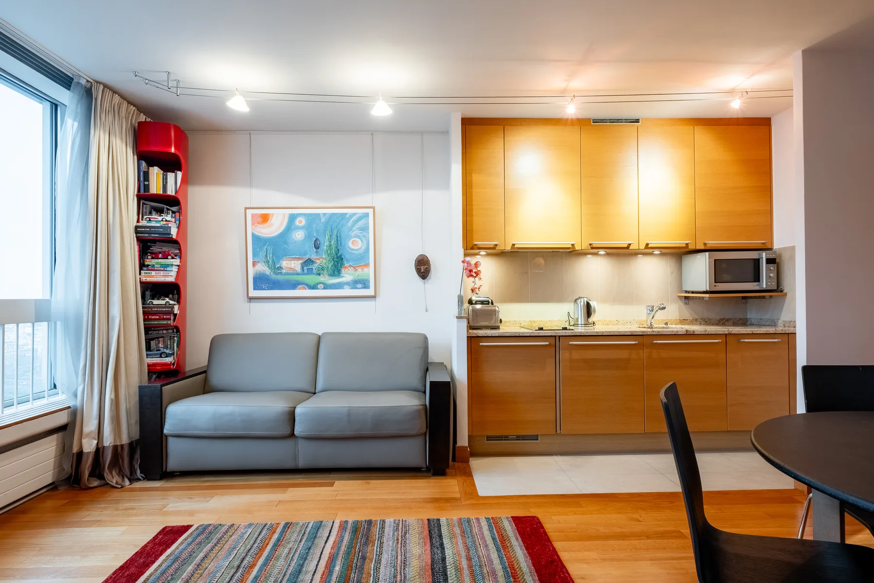 A living area with a gray sofa beside a compact kitchen.