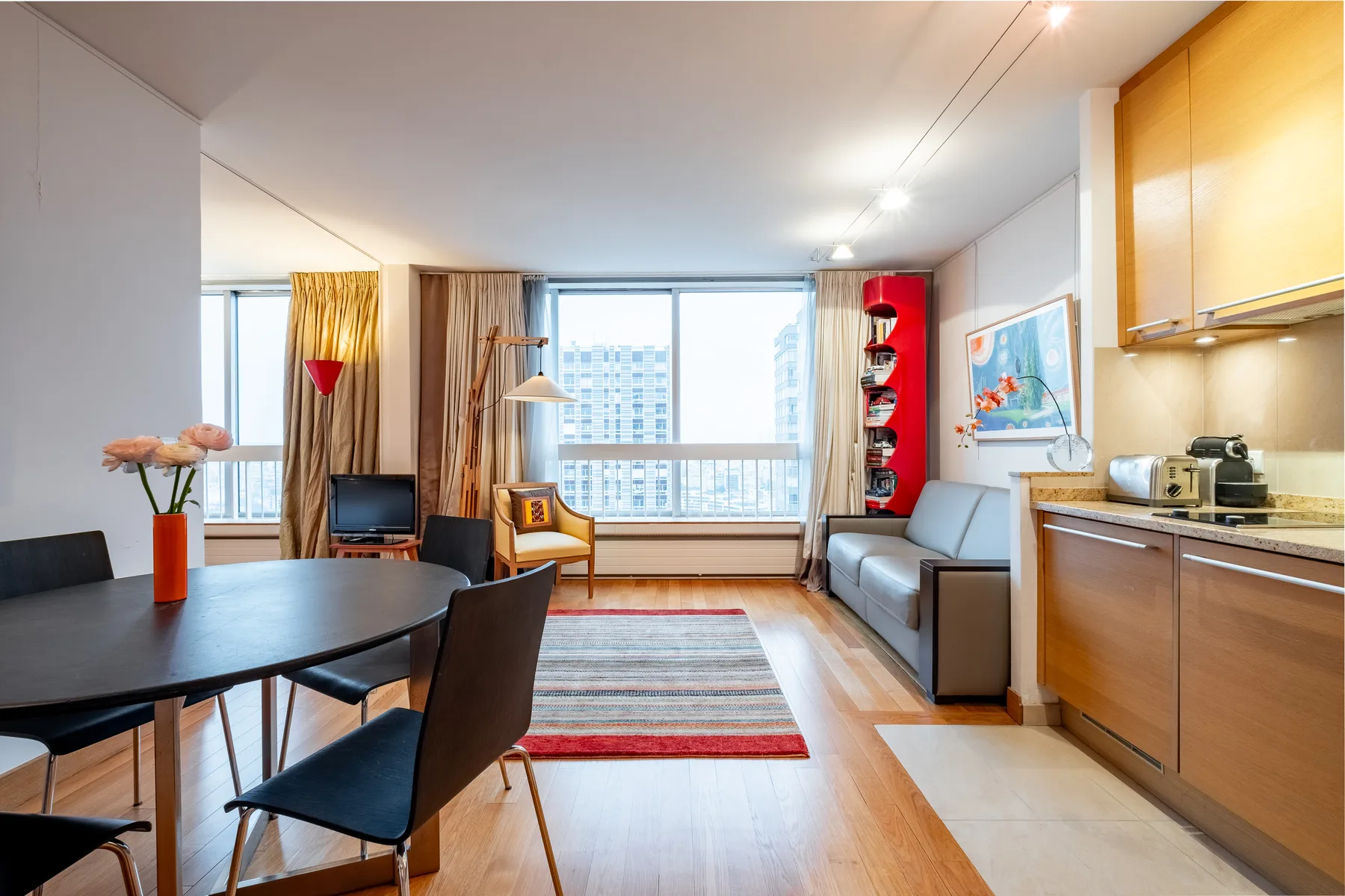 A bright living and dining area with a sofa, table, and large windows.