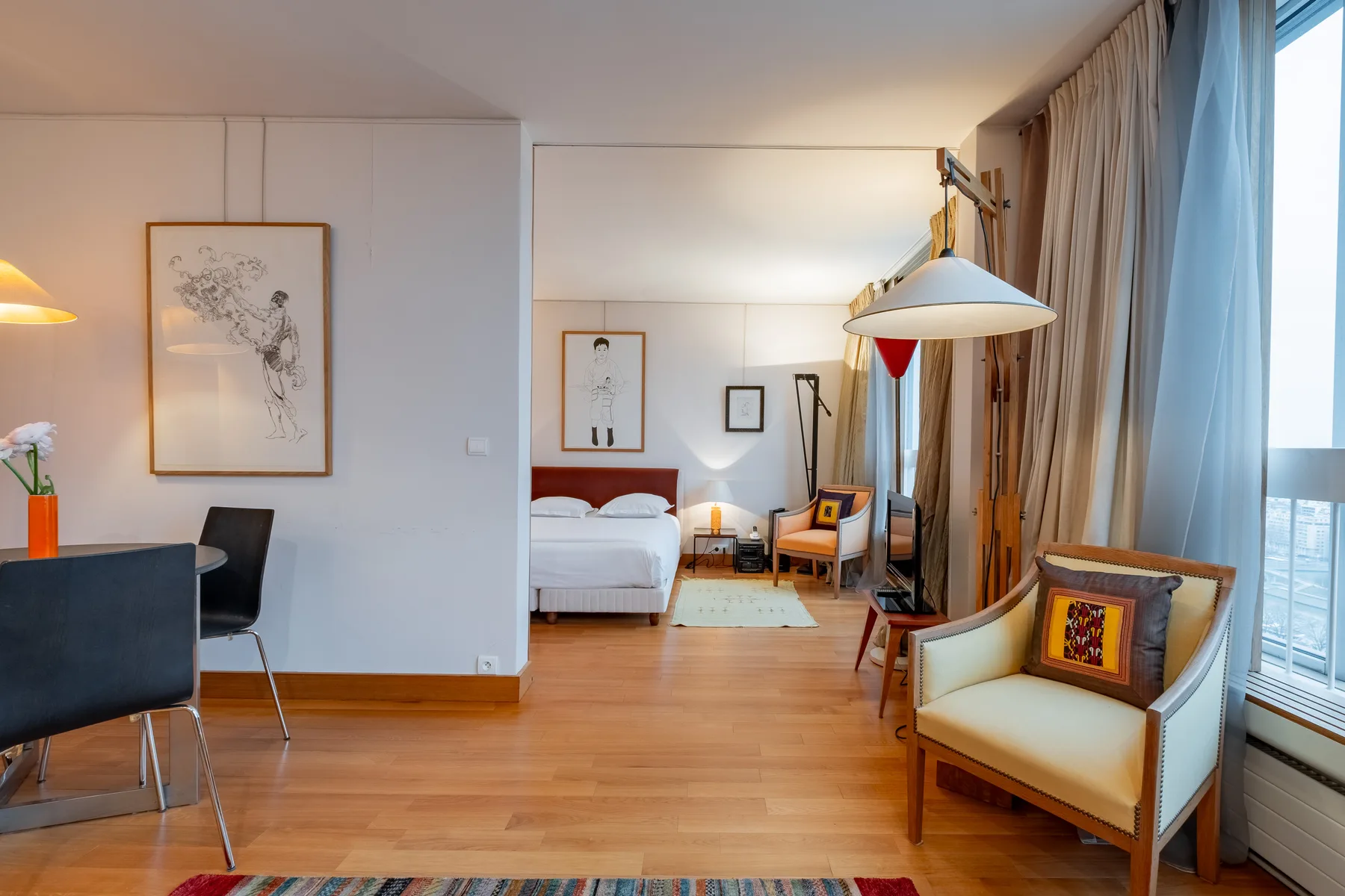 A bright bedroom with a bed, seating area, and large windows.