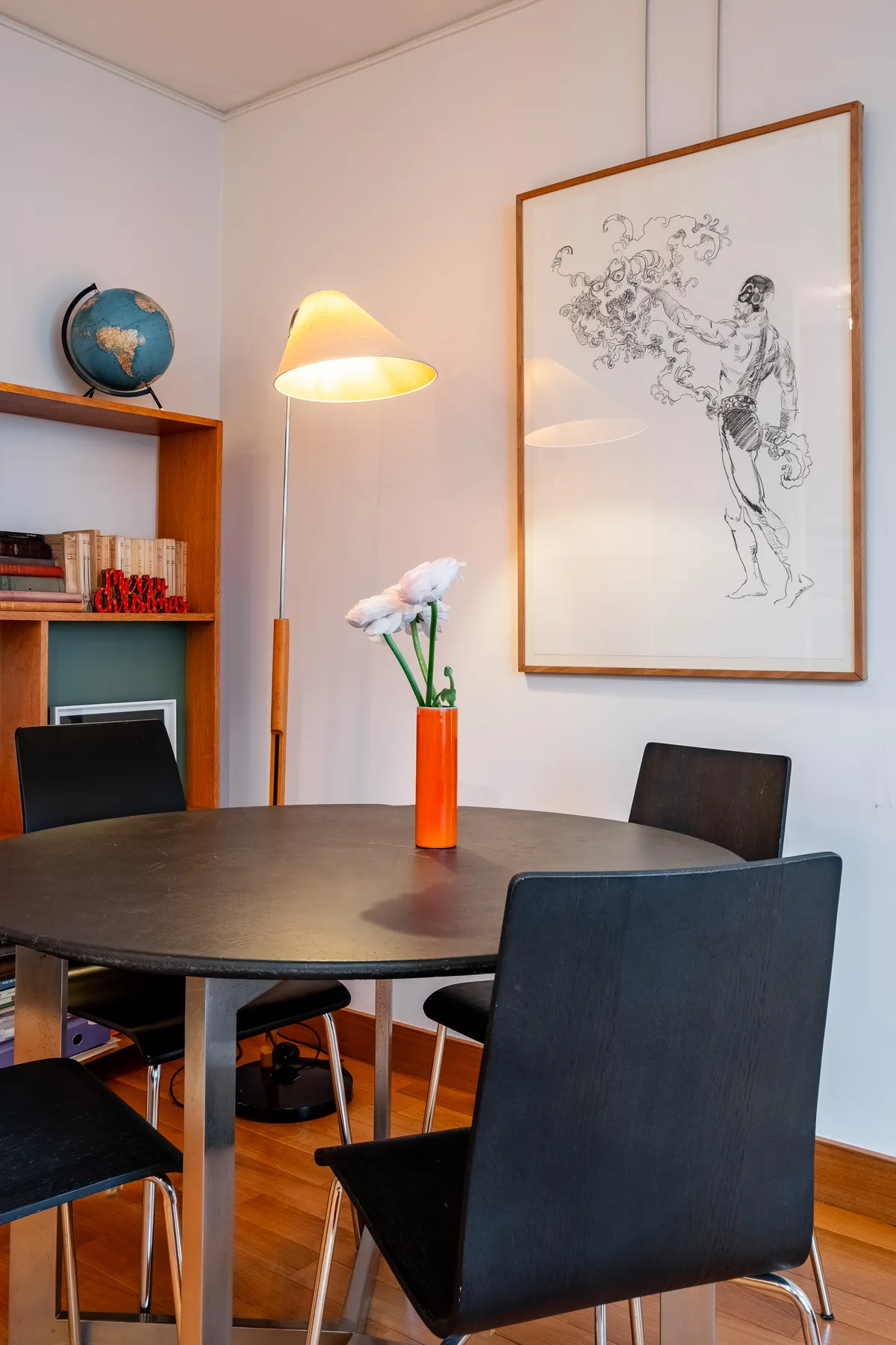 A dining table with dark seating, a floor lamp, and framed artwork.