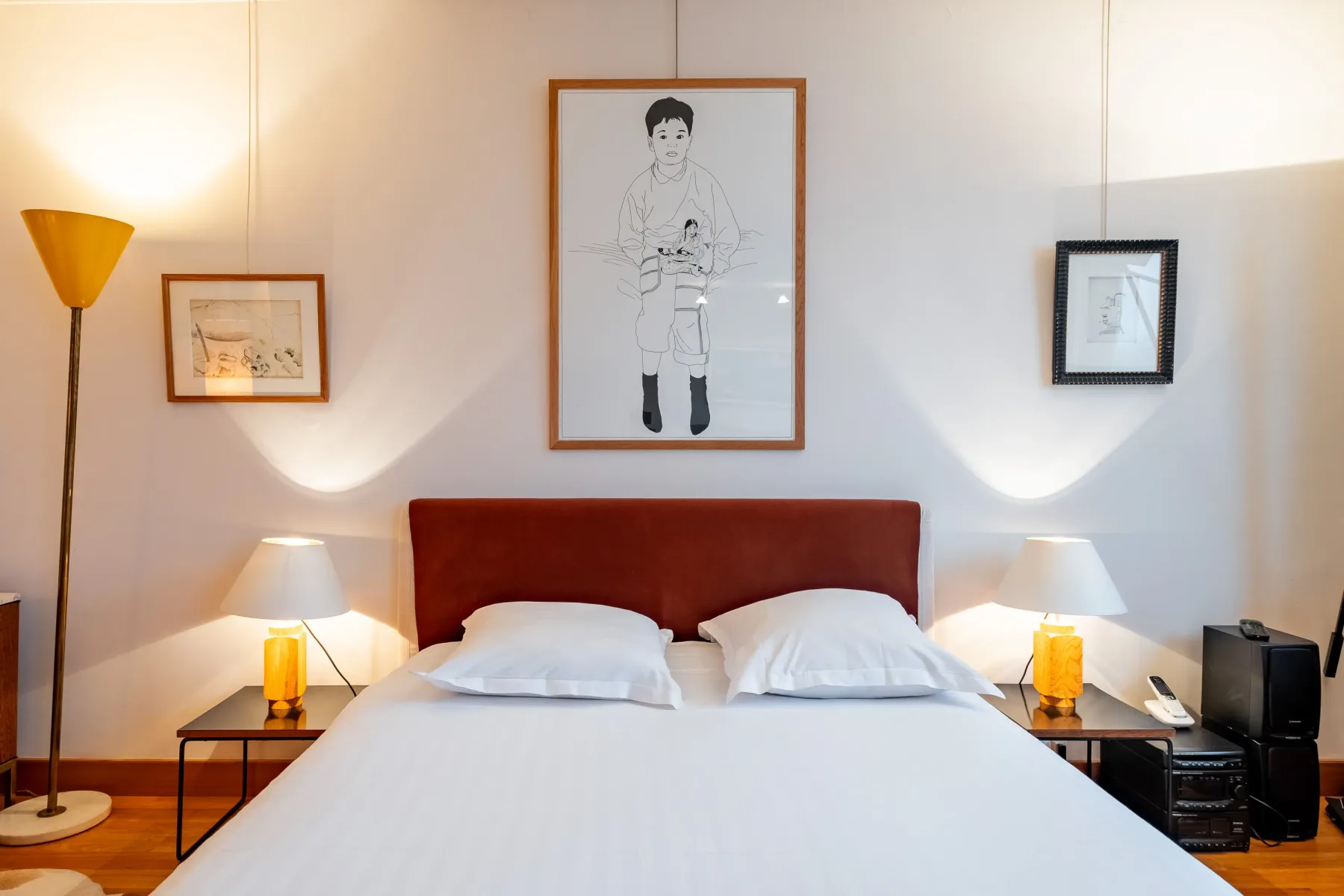A bedroom with a neatly made bed and framed artwork above the headboard.
