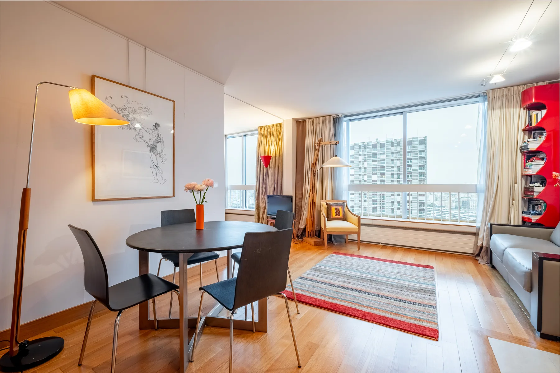 A bright living and dining area with a large window overlooking nearby buildings.
