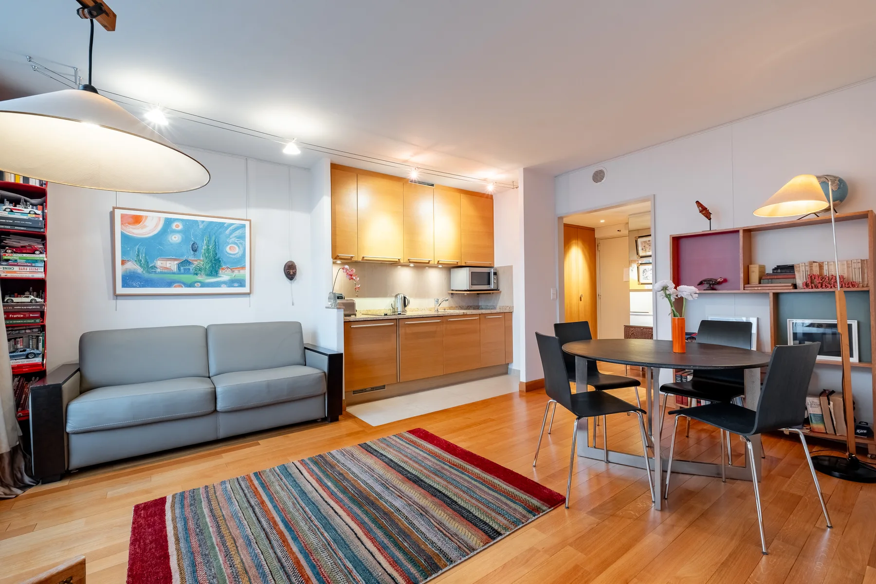 A bright open-plan living and dining area with a gray sofa and wooden kitchen cabinets.