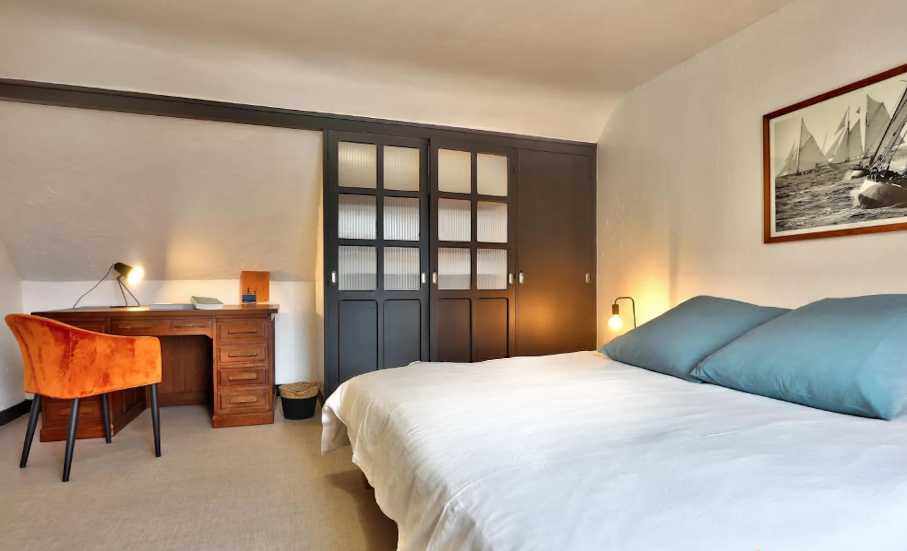 A bedroom with a bed, desk, and dark paneled wardrobe.