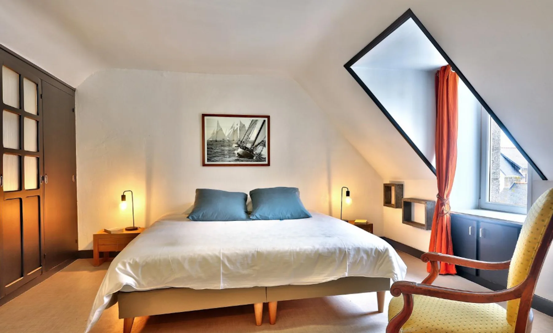 A bedroom with a bed, bedside lamps, and a window.