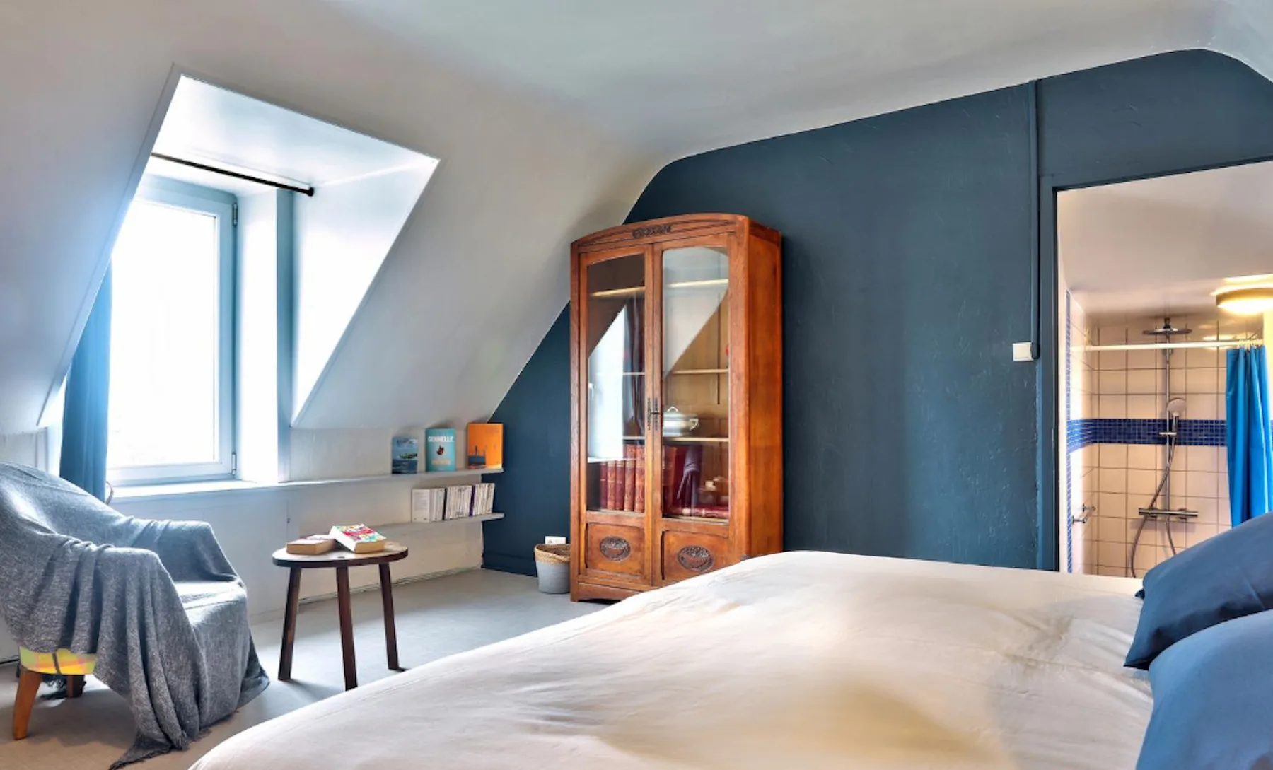 A bedroom with a bed, seating, and a glass-front cabinet.