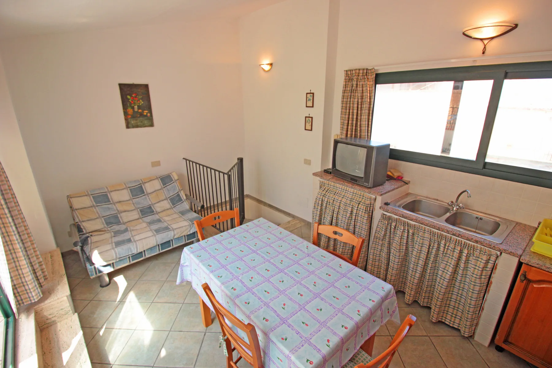 Un comedor con una mesa, asientos y una pequeña cocina junto a la ventana.