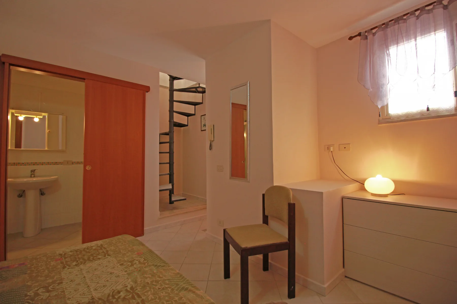 Un dormitorio con una cama, una silla y un escritorio junto a una ventana con cortinas.