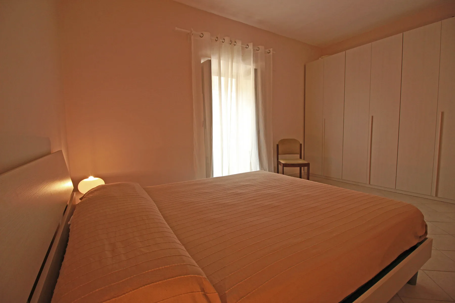 Un dormitorio con una cama bien tendida y una ventana con cortinas.