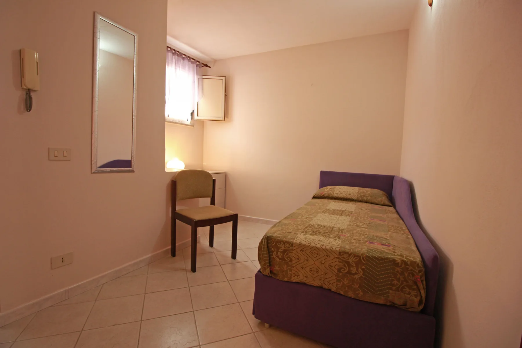 Un dormitorio con una cama individual, una silla y una ventana pequeña.