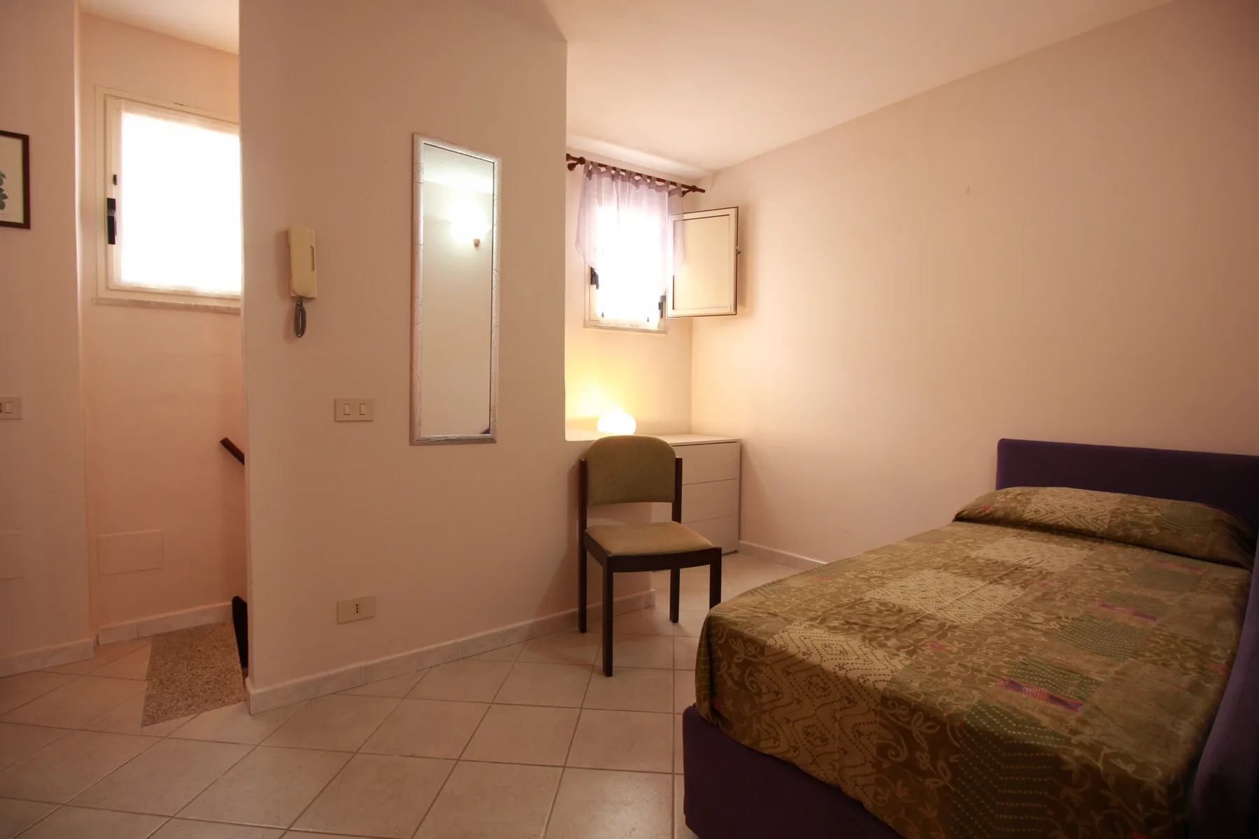 Un dormitorio con una cama, una silla y una ventana pequeña.