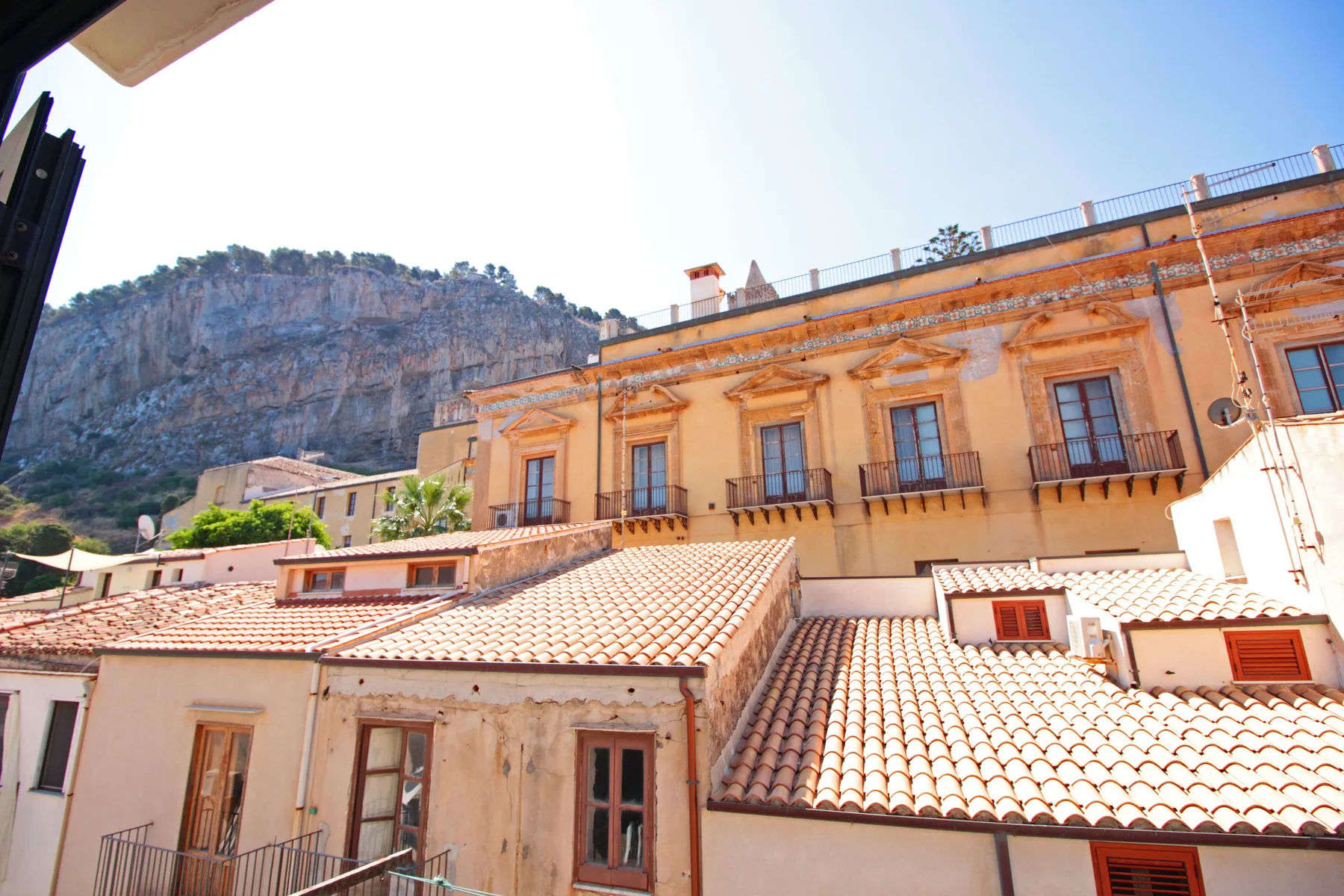 Una vista soleada de edificios en la ladera, con tejados de tejas y una cresta rocosa.