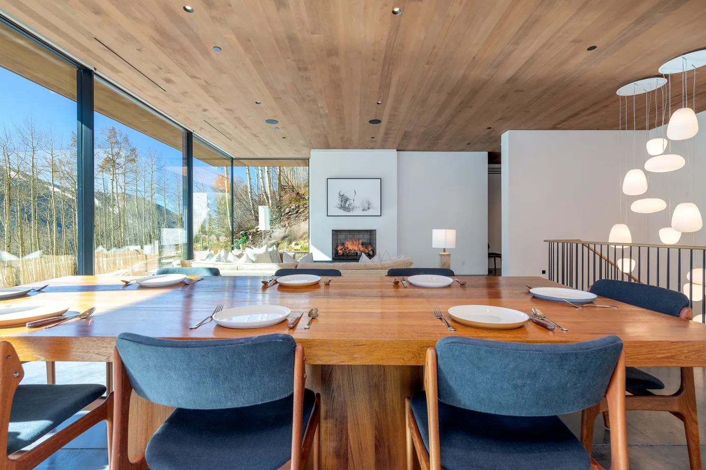 Comedor con una larga mesa de madera junto a ventanales y una chimenea.