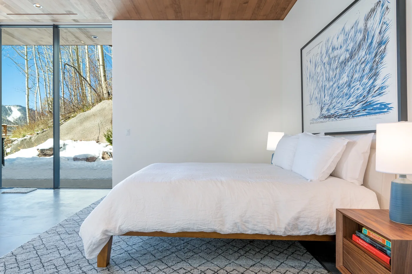 Un dormitorio luminoso con una cama bien tendida junto a una gran puerta de vidrio.