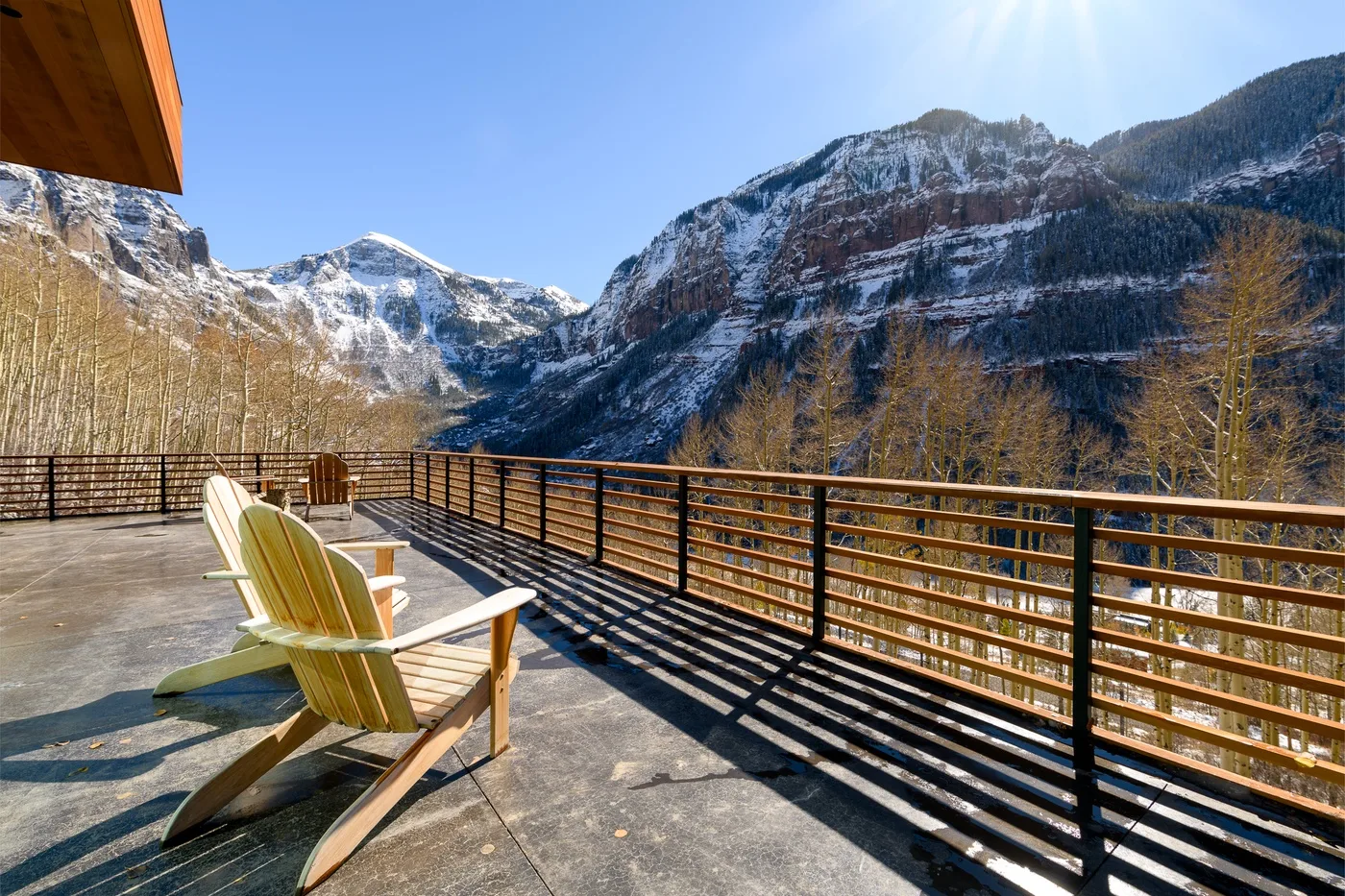 Una terraza con vistas a las montañas, asientos de madera y una barandilla metálica.