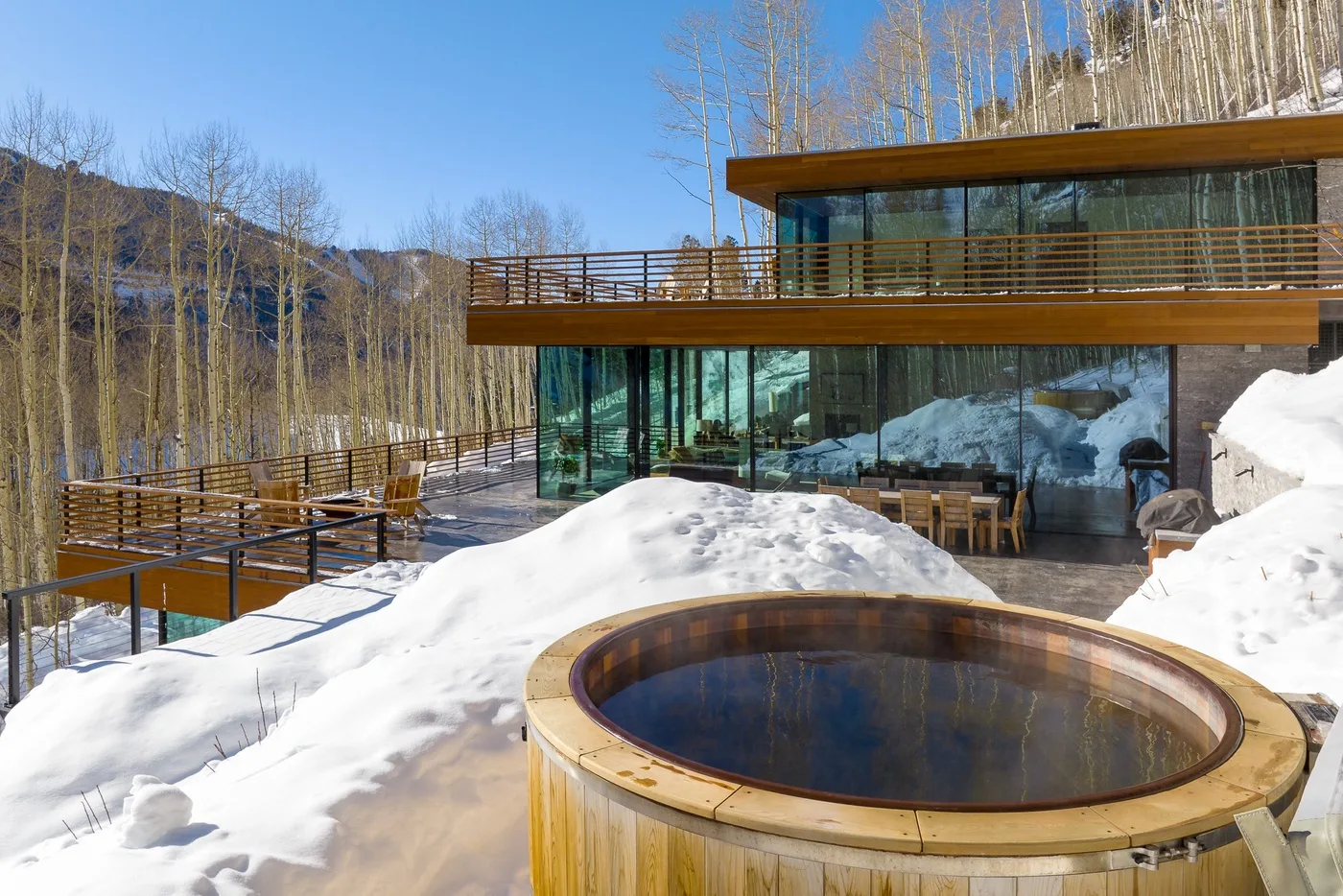 Un edificio moderno con fachada de vidrio y una bañera de hidromasaje redonda al aire libre están rodeados de nieve.