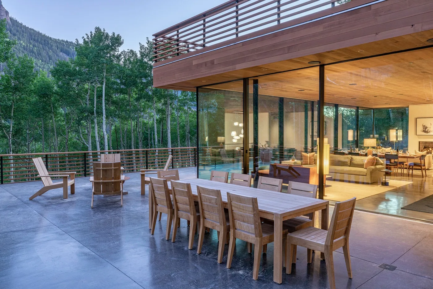 Una casa moderna se abre a una amplia terraza-comedor al aire libre junto a una ladera boscosa.