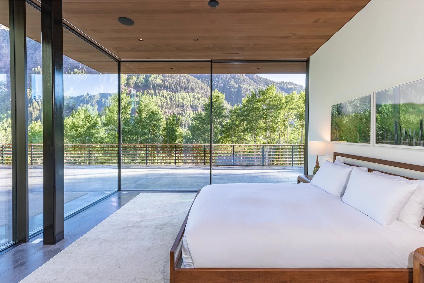 Un dormitorio con una cama junto a ventanales que dan a árboles y montañas.
