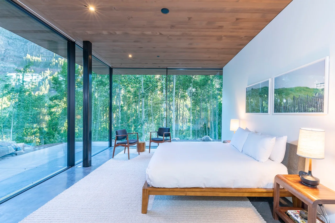 Un dormitorio luminoso con una cama grande junto a ventanales con vistas a los árboles.