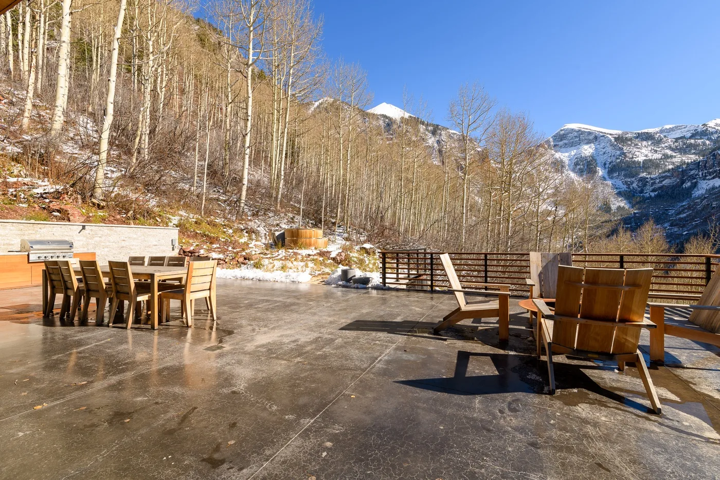 Un patio al aire libre con asientos de madera da a un paisaje montañoso nevado.