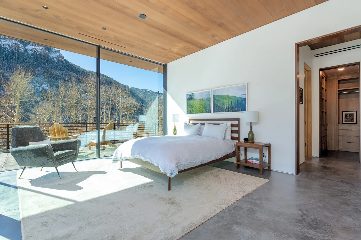 Un dormitorio luminoso con una cama junto a ventanales que dan a un paisaje montañoso.