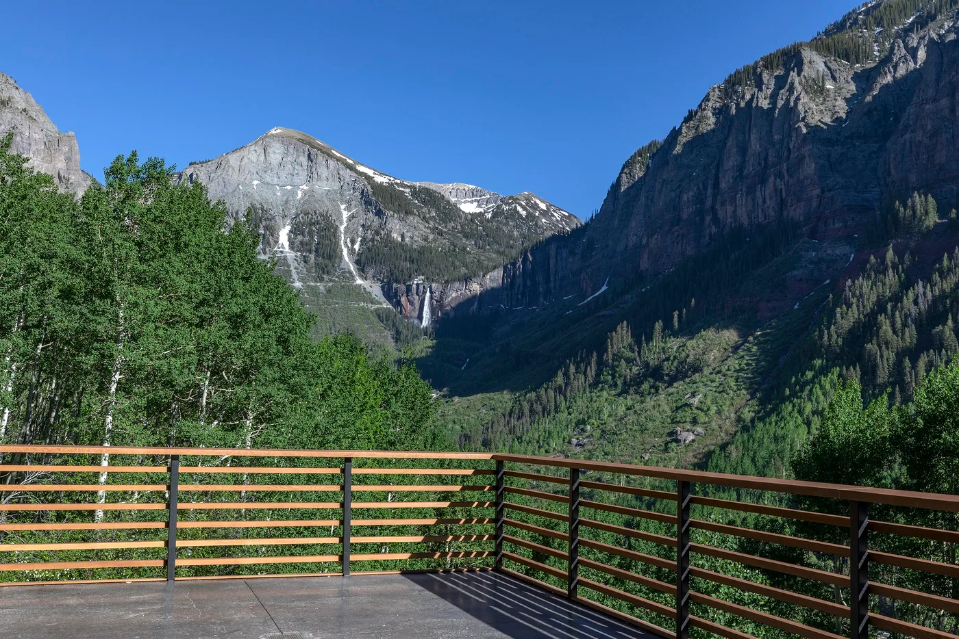 Un valle montañoso y una cascada se ven más allá de la barandilla de una terraza.