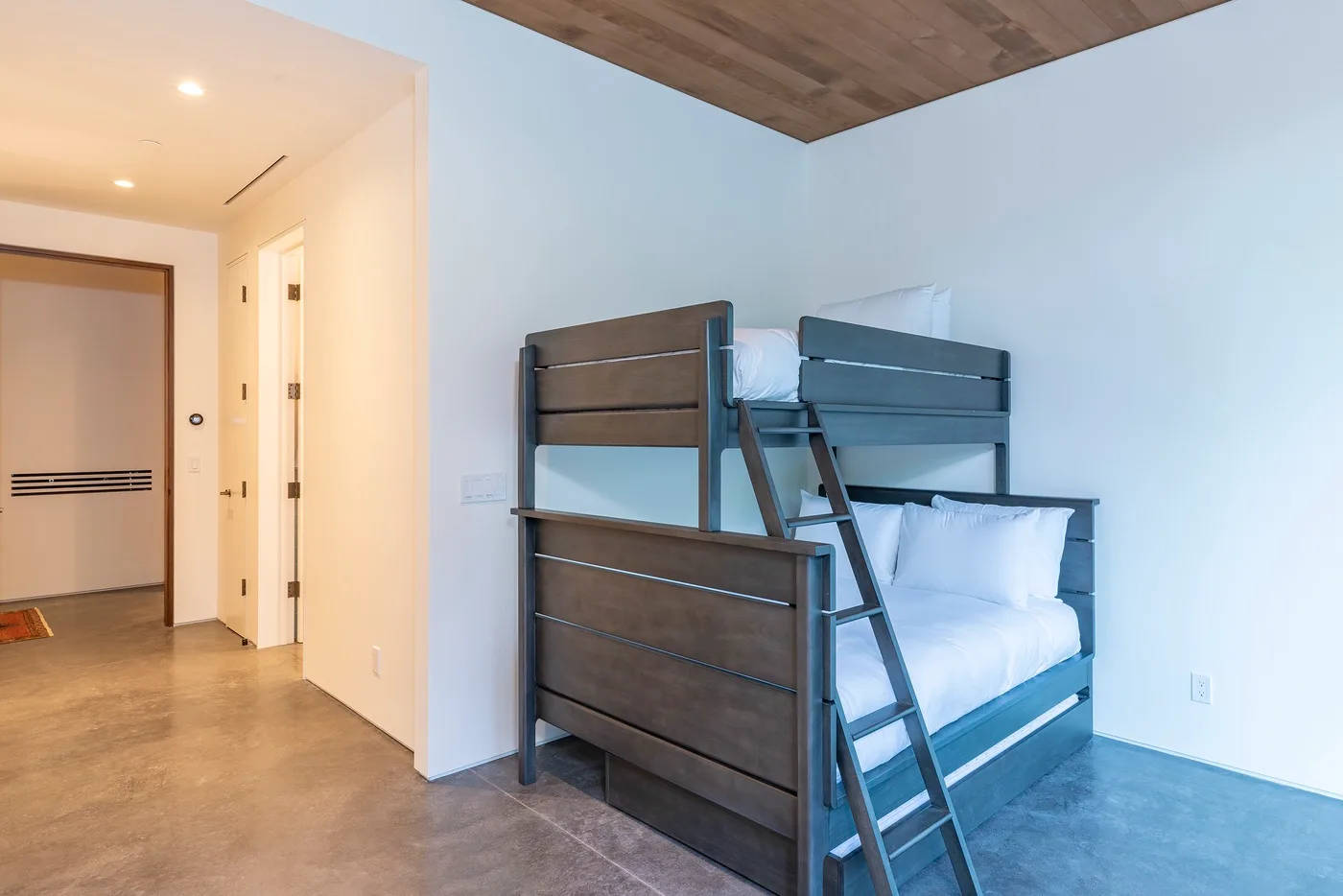Una litera con ropa de cama blanca está junto a una pared clara en un dormitorio.