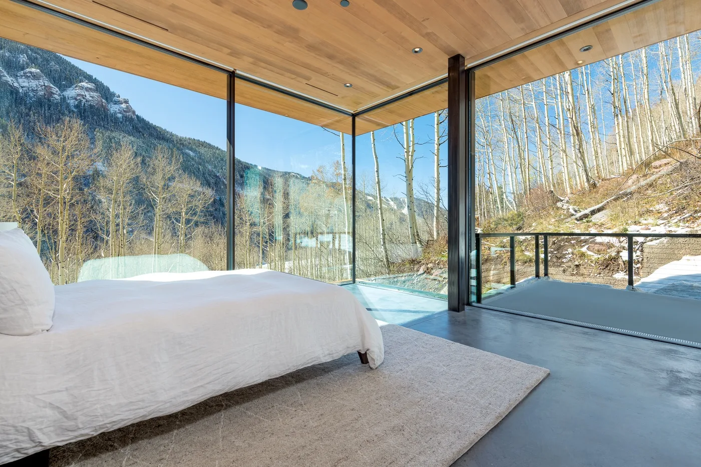 Un dormitorio con una cama junto a ventanales con vistas a un paisaje montañoso y boscoso.
