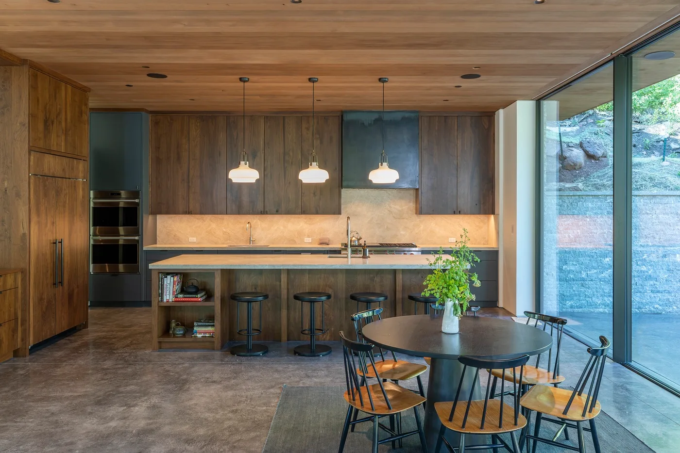 Una cocina y comedor modernos con muebles de madera y una mesa junto a grandes ventanales.