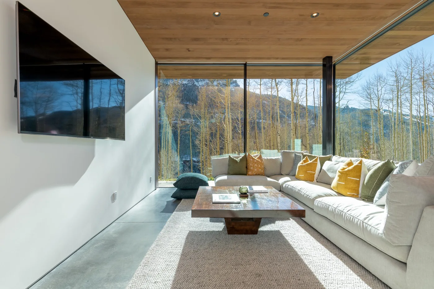 Una sala luminosa con un sofá seccional y grandes ventanas con vistas a los árboles.