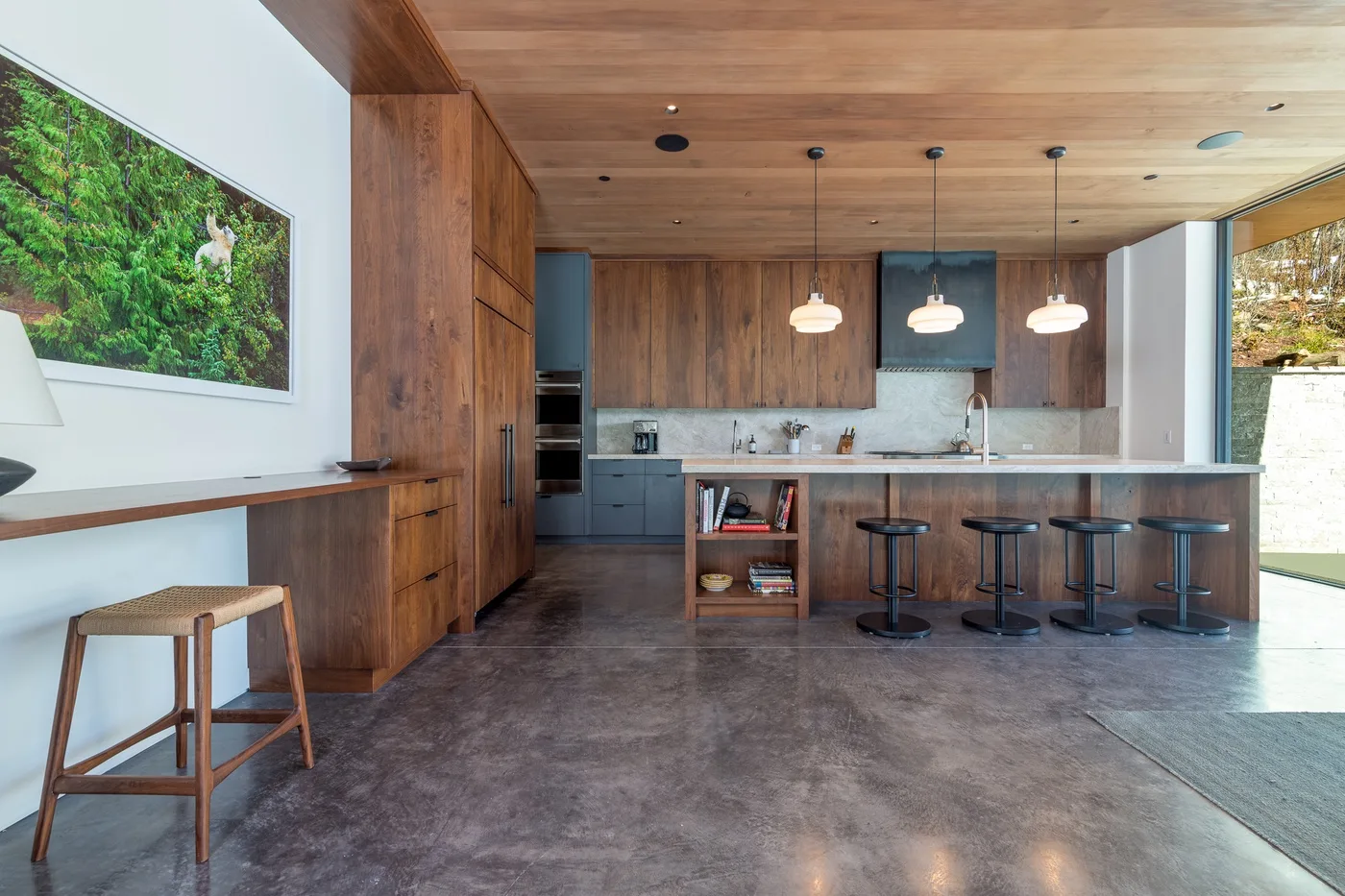 Cocina abierta con una isla larga y taburetes bajo lámparas colgantes.